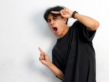 Siyah tişörtlü komik Asyalı genç adamın portresi beyaz arka planda izole edilmiş bir reklam için boş yeri işaret ediyor..