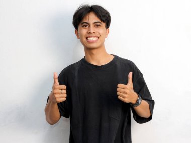 Siyah tişört giyen Asyalı genç bir adamın beyaz arka planda izole edilmiş, baş parmak hareketi gösteren komik bir portresi..