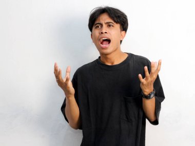 Siyah tişört giyen Asyalı genç bir adamın beyaz arka planda izole edilmiş bir şeye tepki göstermesinin komik bir portresi.