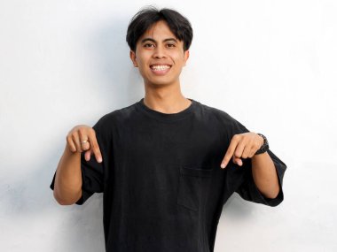 Beyaz arka planda izole edilmiş bir reklam için siyah tişört giyen Asyalı genç bir adamın portresi boş yeri işaret ediyor..