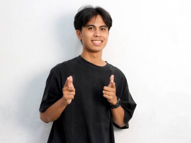 Siyah tişörtlü komik Asyalı genç adamın portresi beyaz arka planda izole edilmiş bir reklam için boş yeri işaret ediyor..