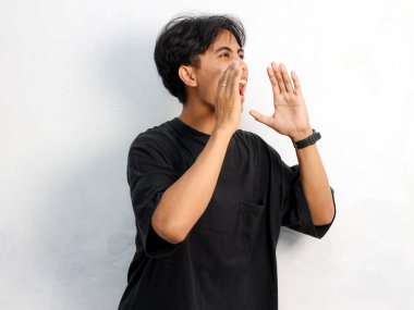 Siyah tişört giyen, kulaklarını elleriyle kapatan ve beyaz arka planda izole edilmiş bağıran Asyalı bir adamın portresi..