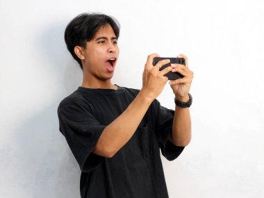 Siyah tişörtlü, cep telefonu tutan Asyalı bir adamın beyaz arka planda izole edilmiş komik bir portresi.