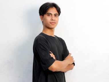 Siyah tişört giyen Asyalı bir adamın portresi, kendine güvenen bir poz veriyor, elleri katlı, beyaz bir arka planda izole edilmiş..