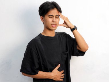 Siyah tişört giyen, beyaz arka planda karnı ağrıyan, yorgun ve üzgün Asyalı genç adamın portresi..