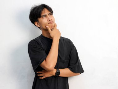 Siyah tişört giyen Asyalı genç adamın ciddi bir portresi. Düşünce ya da kafa karışıklığı içinde beyaz arka planda izole edilmiş..
