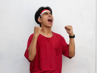 Endonezya 'nın bağımsızlık gününü 17 Ağustos' ta kutlarken çarpıcı kırmızı giysiler giymiş ve ellerini kaldırmış bir Endonezya bayrağı takmış Asyalı genç bir adamın portresi..