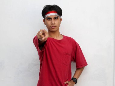 Genç bir Asyalı 'nın portresi, kameraya bakan, dikkat çekici kırmızı bir tişört giyen ve Endonezya bayrağı bandı takan ciddi bir yüzü gösteriyor. Endonezya' nın bağımsızlığını kutlayan bir başlık..