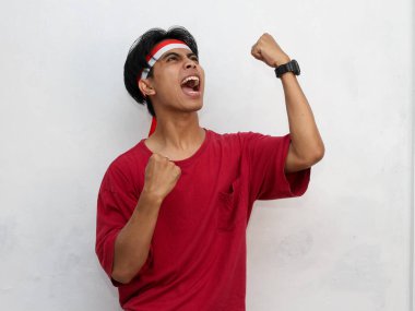 Endonezya 'nın bağımsızlık gününü 17 Ağustos' ta kutlarken çarpıcı kırmızı giysiler giymiş ve ellerini kaldırmış bir Endonezya bayrağı takmış Asyalı genç bir adamın portresi..