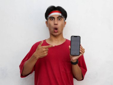 Asya 'lı bir gencin portresi, elinde akıllı bir telefon, dikkat çekici kırmızı bir gömlek ve Endonezya bayrağı takıyor. 17 Ağustos' ta Endonezya 'nın bağımsızlık kutlamaları var..