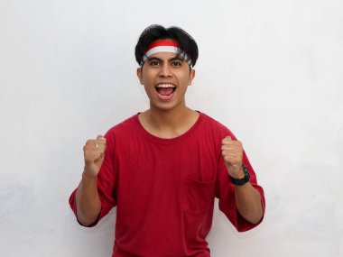 Endonezya bayrağı taşıyan kırmızı tişört ve saç bandı takan Asyalı bir gencin portresi. Endonezya 'nın 17 Ağustos' taki bağımsızlığını coşkuyla kutlayan.