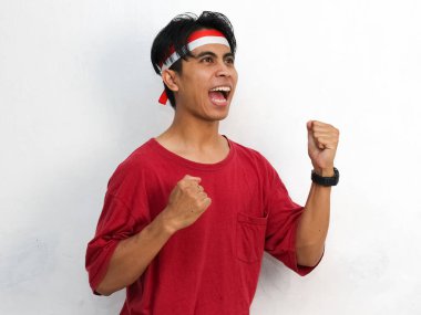 Endonezya 'nın bağımsızlık gününü 17 Ağustos' ta kutlarken çarpıcı kırmızı giysiler giymiş ve ellerini kaldırmış bir Endonezya bayrağı takmış Asyalı genç bir adamın portresi..