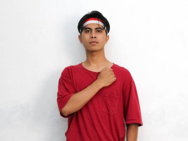 Asyalı gururlu genç bir adamın portresi, çarpıcı kırmızı bir gömlek ve Endonezya bandı takıyor. 17 Ağustos 'ta Endonezya' nın bağımsızlığını kutlayan ellerini göğsüne koy.