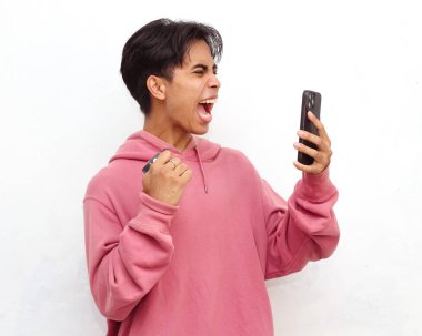 Çok heyecanlı genç Asyalı bir adamın portresi, pembe kapüşonlu, elinde akıllı telefon ve ATM kartı, beyaz arka planda izole edilmiş..