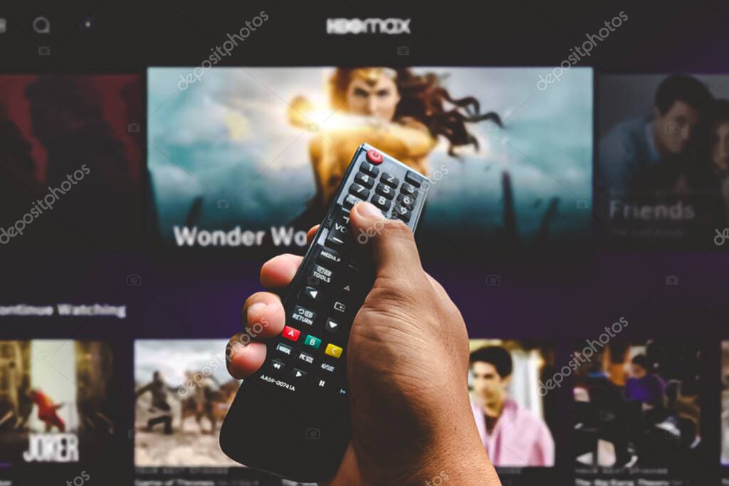 Man with TV remote control in hand and HBOmax logo in background. HBOmax is the global provider of streaming movies and TV series.Indonesia - June 13th 2024.
