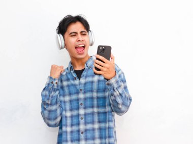 Stüdyoda akıllı telefonla poz veren kulaklık takan genç Asyalı adam.