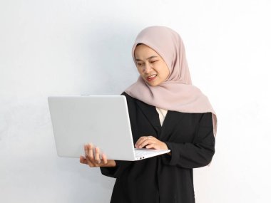 Genç Müslüman kadın tesettür takıyor ve dizüstü bilgisayarını beyaz arka planda tutuyor.