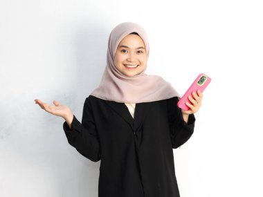 Stüdyoda akıllı telefonla poz veren tesettürlü genç Asyalı Müslüman kadın.