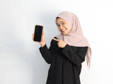 Stüdyoda akıllı telefonla poz veren tesettürlü genç Asyalı Müslüman kadın.