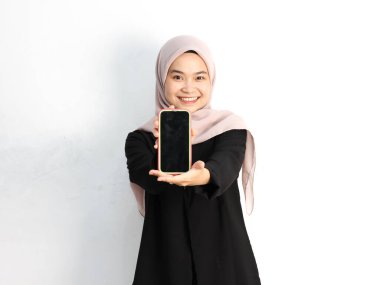 Stüdyoda akıllı telefonla poz veren tesettürlü genç Asyalı Müslüman kadın.