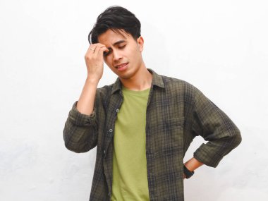 Beyaz arka planda yeşil flanel gömlekli sinirli Asyalı adam poz veriyor.    