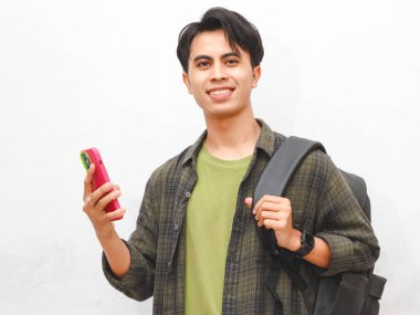 Yeşil flanel gömlekli Asyalı adam beyaz arka planda akıllı telefon tutuyor.  