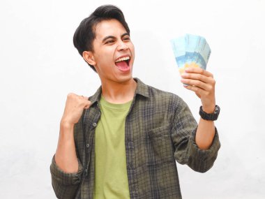 Yeşil flanel gömlekli Asyalı adam beyaz arka planda para tutuyor.  