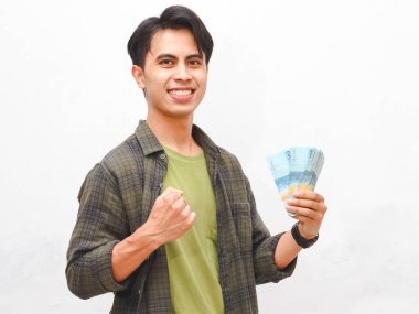 Yeşil flanel gömlekli Asyalı adam beyaz arka planda para tutuyor.  