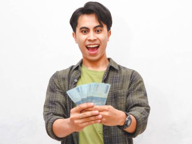 Yeşil flanel gömlekli Asyalı adam beyaz arka planda para tutuyor.  