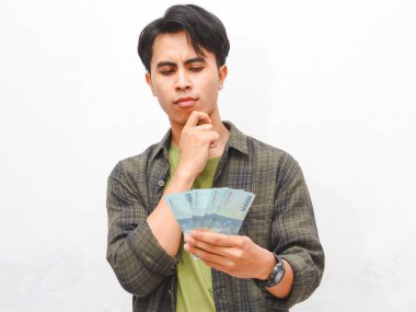 Yeşil flanel gömlekli Asyalı adam beyaz arka planda para tutuyor.  