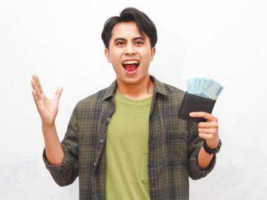 Yeşil flanel gömlekli Asyalı adam, beyaz arka planda parası olan bir cüzdan taşıyor.  