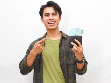 Yeşil flanel gömlekli Asyalı adam, beyaz arka planda parası olan bir cüzdan taşıyor.  