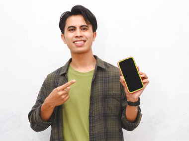 Yeşil flanel gömlekli Asyalı adam beyaz arka planda akıllı telefon tutuyor.  