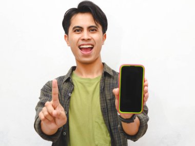 Yeşil flanel gömlekli Asyalı adam beyaz arka planda akıllı telefon tutuyor.  