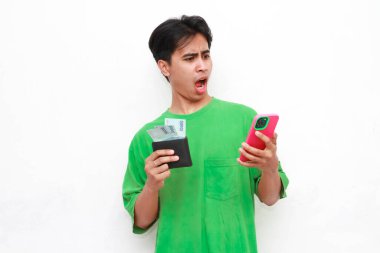 Yeşil tişörtlü neşeli yetişkin bir Asyalı elinde akıllı telefon ve cüzdan beyaz arka planda izole edilmiş parayla poz veriyor.