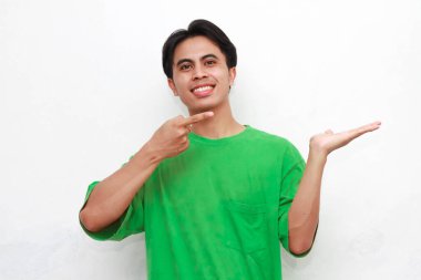Yeşil tişörtlü neşeli yetişkin Asyalı adam beyaz arka planda avuç içini gösteriyor.