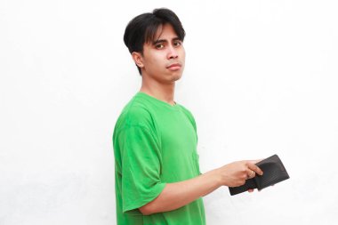 Zavallı Asyalı adam yeşil tişörtlü, elinde boş bir cüzdan olan üzgün, stresli yüzünü beyaz arka planda gösteren bir adam.