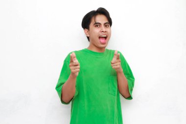 Yeşil tişörtlü neşeli yetişkin Asyalı adam beyaz arka planda izole edilmiş boş bir bölgeyi işaret ediyor.