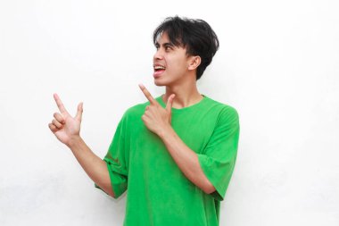 Yeşil tişörtlü neşeli yetişkin Asyalı adam beyaz arka planda izole edilmiş boş bir bölgeyi işaret ediyor.