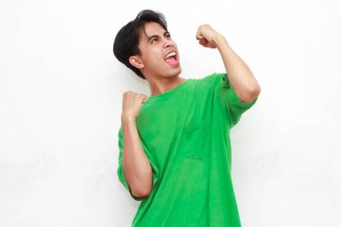 Yeşil tişörtlü neşeli, yetişkin Asyalı adam beyaz bir arka planda heyecanlı bir ifadeyle iki eliyle poz veriyor..