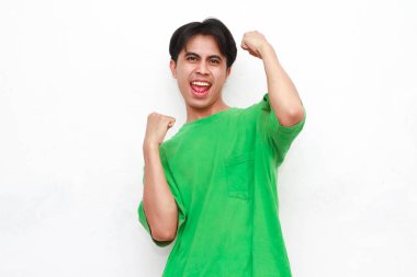 Yeşil tişörtlü neşeli, yetişkin Asyalı adam beyaz bir arka planda heyecanlı bir ifadeyle iki eliyle poz veriyor..
