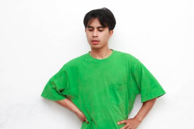 Yeşil tişörtlü üzgün, Asyalı bir adam beyaz arka planda stresli bir hareketle poz veriyor.