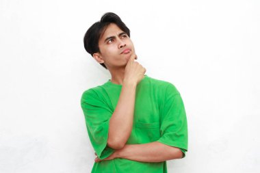 Yeşil tişörtlü üzgün, Asyalı bir adam beyaz arka planda stresli bir hareketle poz veriyor.