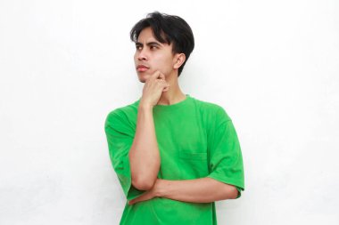 Yeşil tişörtlü üzgün, Asyalı bir adam beyaz arka planda stresli bir hareketle poz veriyor.
