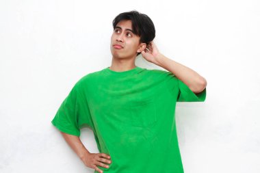 Yeşil tişörtlü üzgün, Asyalı bir adam beyaz arka planda stresli bir hareketle poz veriyor.