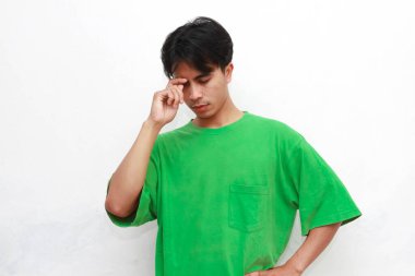 Yeşil tişörtlü üzgün, Asyalı bir adam beyaz arka planda stresli bir hareketle poz veriyor.