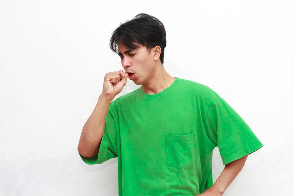 Unhealthy adult Asian man in green t-shirt posing coughing on white background.