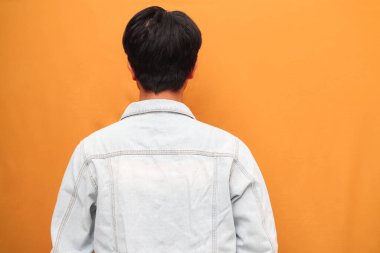 Asyalı bir adamın arkadan görünüşü, Asyalı genç bir adamın sarı arka planda izole edilmiş bir tarafı işaret etmesi.