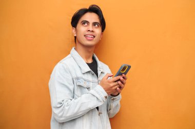 Akıllı telefonu işaret eden mutlu Asyalı genç adam. Akıllı telefonu tutan neşeli Asyalı genç adam. Sarı arka planda izole edilmiş bir tarafa bakıyor..