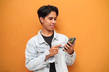 Akıllı telefonu işaret eden mutlu Asyalı genç adam. Akıllı telefonu tutan neşeli Asyalı genç adam. Sarı arka planda izole edilmiş bir tarafa bakıyor..
